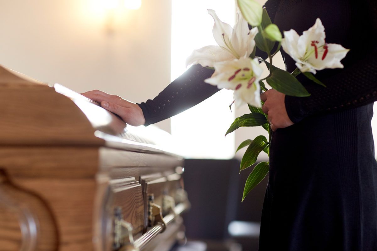 woman-with-lily-flowers-and-coffin-at-funeral-PM62BEU